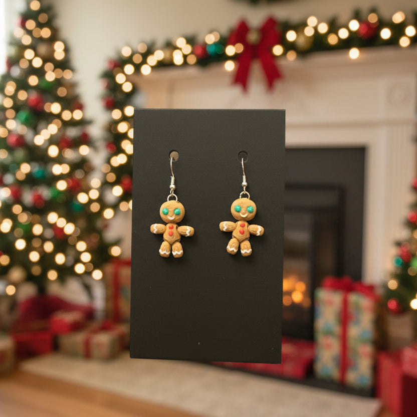 Pair of gingerbread man earrings displayed on a black card with Christmas decorations in the background.