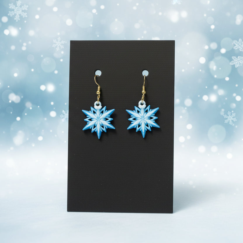 Blue snowflake earrings on a black card with a snowy background
